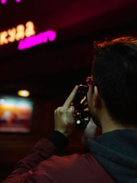 Rear view of man photographing with smart phone at night