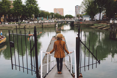 Rear view of woman standing on footpath leading towards pier at river