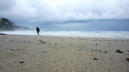 Rear view of man walking on beach against sky