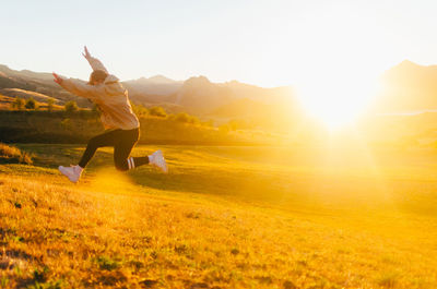 Back view of unrecognizable male in casual clothes jumping high against mountains