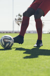 Lower half of african american football player kicking a ball on grass