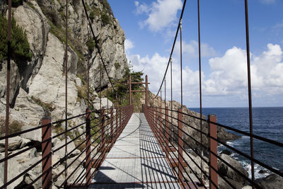 Footbridge by mountain against cloudy sky