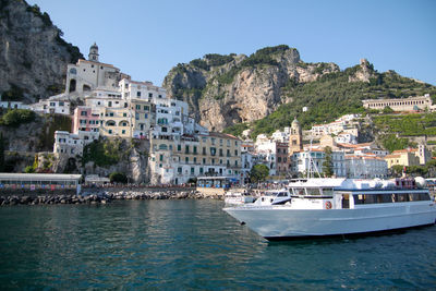 Sailboats moored on sea by buildings in city against clear sky