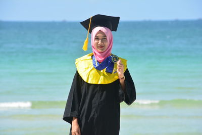 Portrait of woman in hijab wearing mortarboard while standing against sea