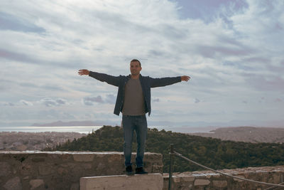 Man with arms outstretched standing on landscape against sky