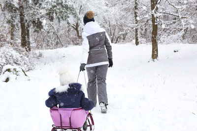 Mom takes his little daughter on a sledge uphill through the winter 