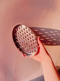 Woman hand holding oval grater which throws shadow on the wall