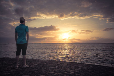 Rear view of man standing on beach against sky during sunset