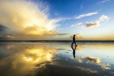 Silhouette person on beach against sky during sunset