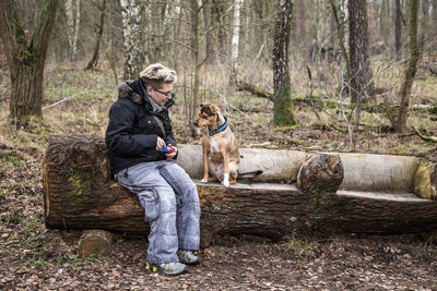 Woman with dog sitting on tree trunk in forest