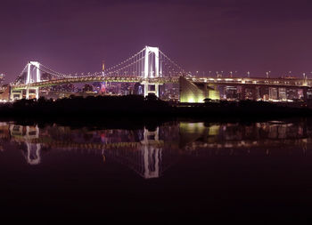 Illuminated bridge over river with city in background at night