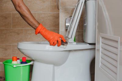 Cropped hands of person cleaning toilet bowl with brush