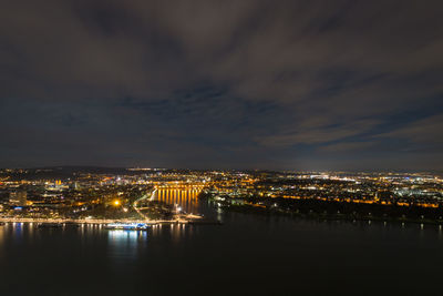 Illuminated buildings by river against sky at night