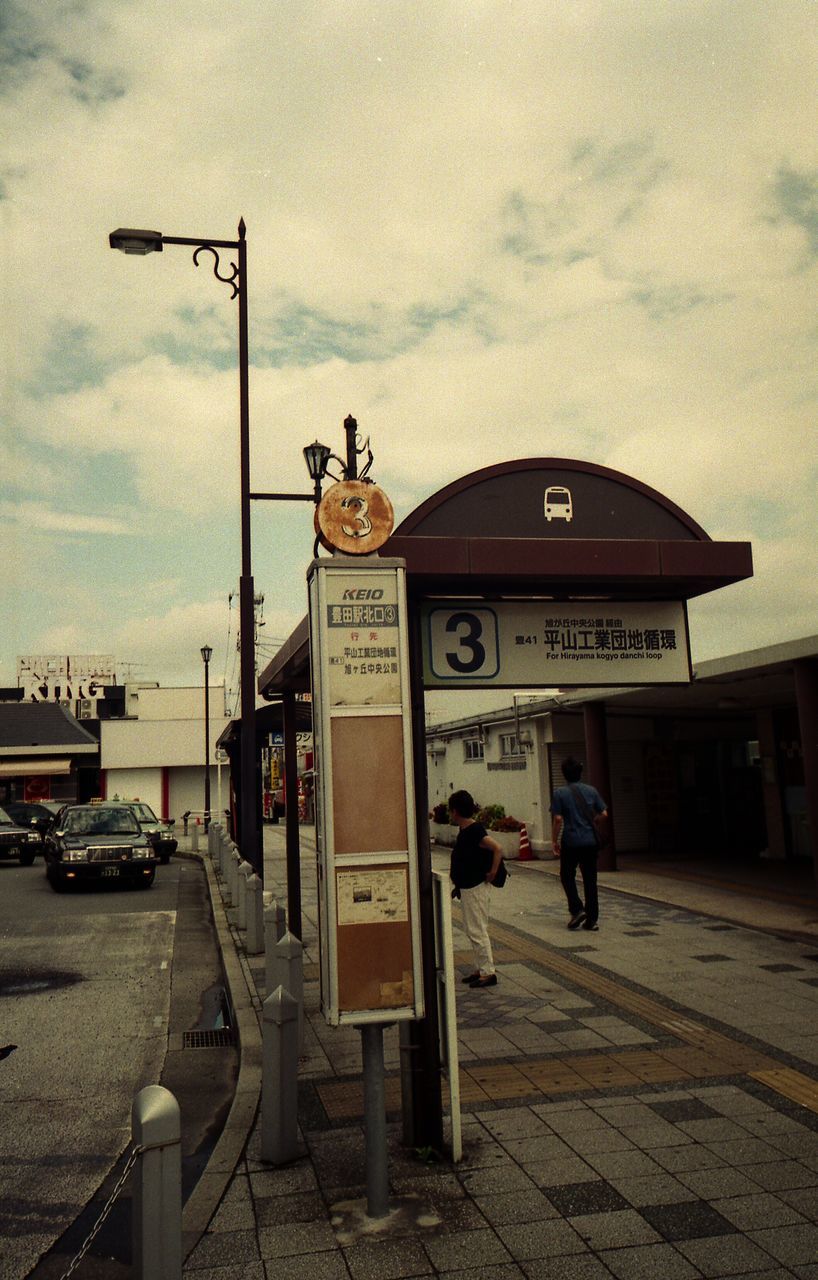 text, western script, communication, sky, built structure, architecture, real people, cloud - sky, outdoors, telephone booth, building exterior, day, city, road sign, men, full length, pay phone, fuel pump, one person, people