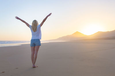 Full length of woman standing on beach against sky during sunset