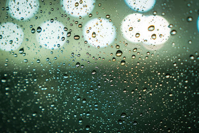 Rain drops on window glass with bokeh lights on the background