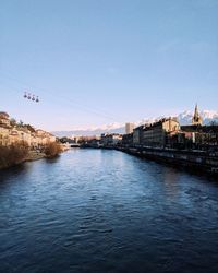 Bridge over river by buildings against clear sky