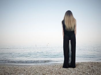 Full length of young woman wearing black dress while standing on shore at beach against sky