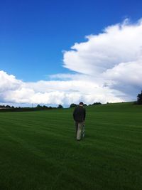 Rear view of man walking on grassy field against cloudy sky