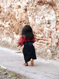 Rear view of woman standing against brick wall