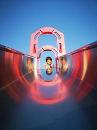 Low angle view of girl on slide in playground against clear blue sky