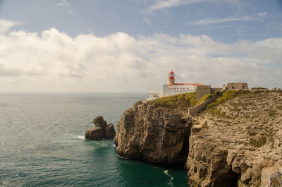 Lighthouse on sea by buildings against sky