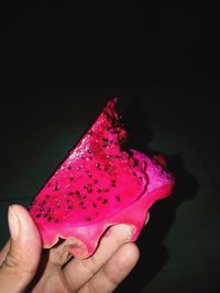 Close-up of hand holding ice cream cone against black background