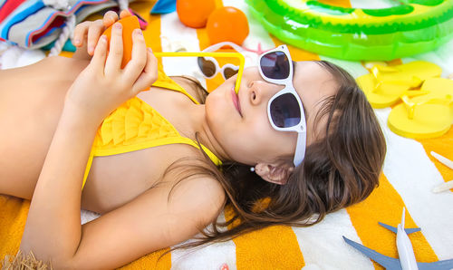 Girl sipping juice from orange fruit through straw lying on towel