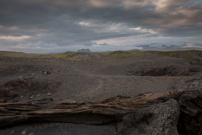 Rock formations at black sand beach against cloudy sky