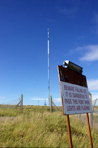Warning sign by radio mast on field against clear blue sky