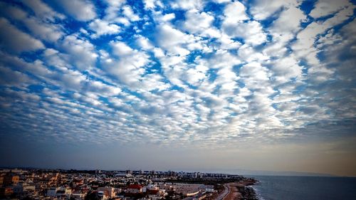 Aerial view of city by sea against cloudy sky