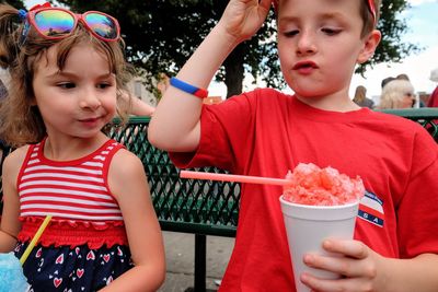 Siblings having flavored ice while sitting on bench