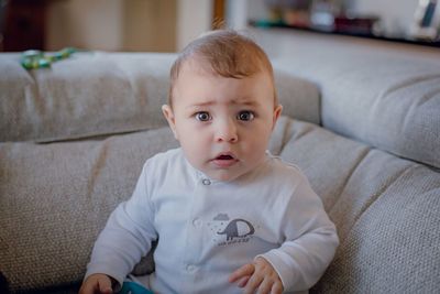 Portrait of cute baby boy sitting on sofa in living room at home