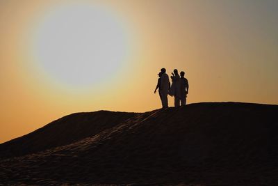 Silhouette people on sand dune against clear sky
