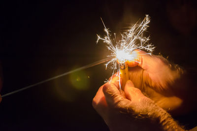 Cropped hands of man igniting sparkler with cigarette lighter at night