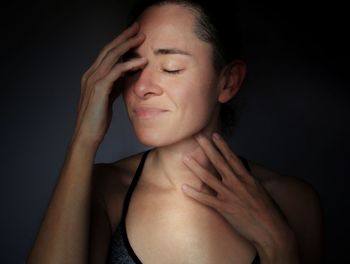 Portrait of young woman touching hair against black background