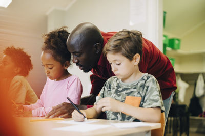 Mid adult teacher assisting students at desk in classroom