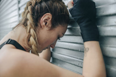 Woman taking break from training while standing against shutter