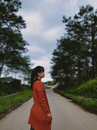 Side view of woman standing on road against trees