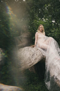 Portrait of young woman sitting on tree in forest