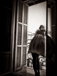 Rear view of woman standing by window at home
