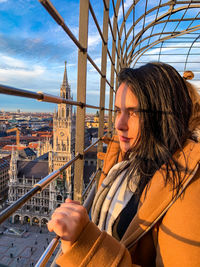 Young woman standing by railing in city against sky