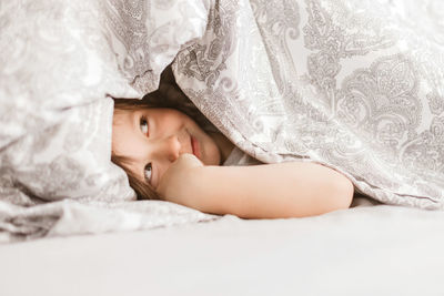 A cute boy of 4 years old looks out from under the blanket. morning fun at home. moments of life.