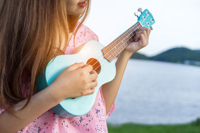 Midsection of woman playing ukulele against lake