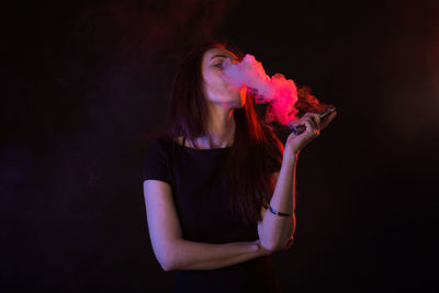 Young woman holding cigarette against black background