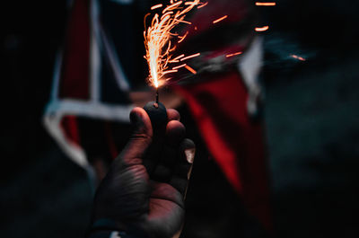 Cropped hand of person holding illuminated firecracker