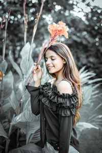 Young woman smiling while holding plant against trees