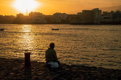 Rear view of man sitting on beach during sunset