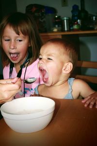 Close-up of two cute little girls eating food at home. mother feeding baby girl with spoon. 