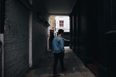 Rear view of man standing on alley amidst buildings